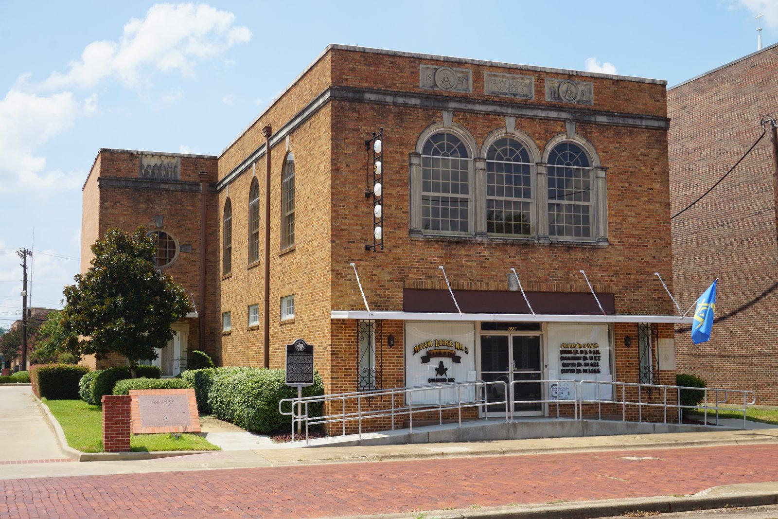 The brick lodge hall of Milam Lodge No. 2 in Nacogdoches, Texas, a two-story 1930s building with arched windows, a Masonic square and compasses on the parapet, and a state historical marker in front.