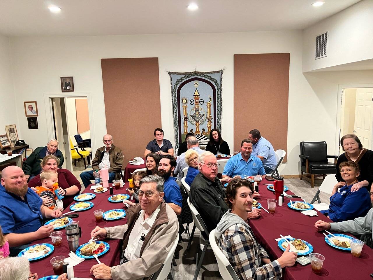 A multi-generational lodge dinner — members, wives, children, and elders gathered around a long table in the dining hall.